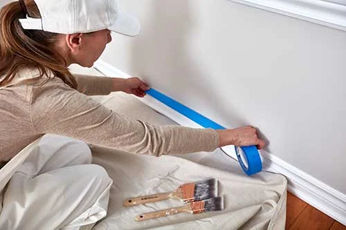 Interior Paint Prep - Painter Applying Painter's Tape Around Base Trim