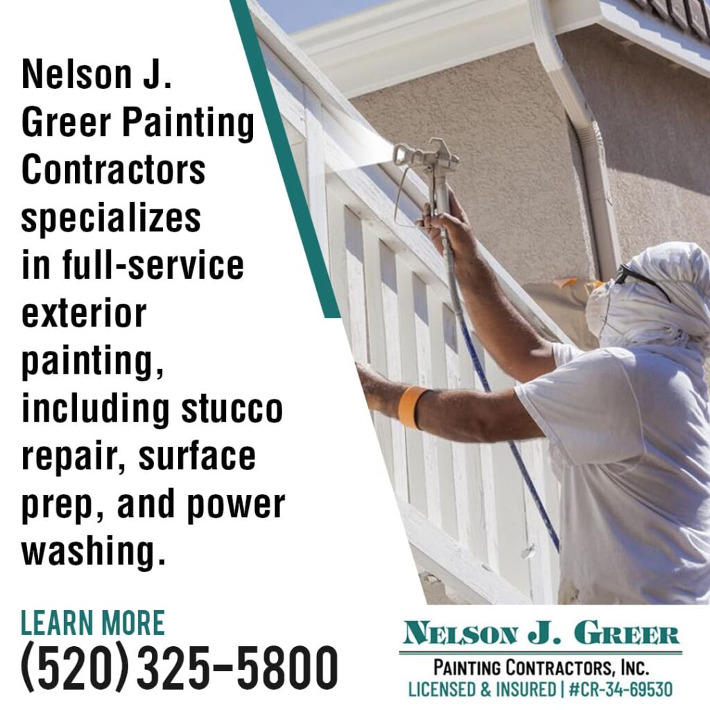 A painter wearing protective gear and using a spray gun to paint the exterior trim of a building.
